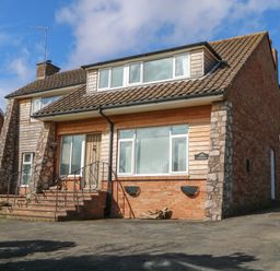 A brick and wood paneled house with steps and metal railing leading to the front door at Casalmare in Exmouth
