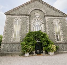 Stone building with arched windows and greenery around the entrance at Capel Mawr Basement 19 in Llanrug