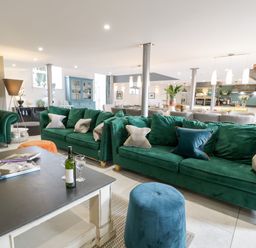 A living area with green sofas a black coffee table with wine and glasses and a blue ottoman at Capel Mawr Basement 19 in Llanrug
