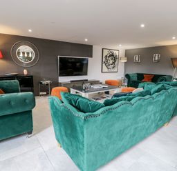 A living room with green sofas orange cushions and poufs a large television and a round mirror at Capel Mawr Basement 19 in Llanrug