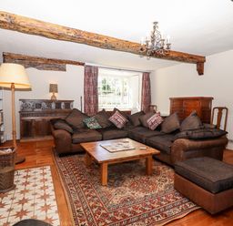 A sitting room with a large sectional sofa a wooden coffee table and exposed wooden beams at Aluric's Hall in Porlock