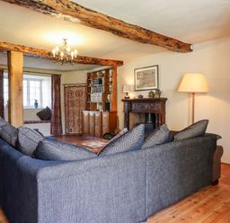 A living room with a large sectional sofa wooden beams a wooden cabinet and a fireplace at Aluric's Hall in Porlock