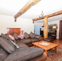 A living room with a brown sectional sofa a wooden coffee table exposed wooden beams and a window at Aluric's Hall in Porlock