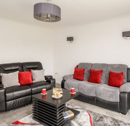 A living room with two sofas a black coffee table with cups and plates and a red floor lamp at Rosamond in Shipton Gorge