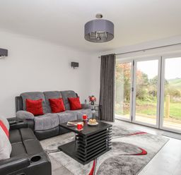 A living room with sofas and red cushions next to large glass doors with a view of greenery at Rosamond in Shipton Gorge