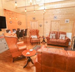 A lounge area with leather armchairs and sofas a wooden coffee table a dining table with chairs and a wall mounted TV at Bryn Derwen Lodge in Bethesda