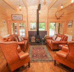 A living room with leather sofas armchairs a wood stove and a rug at Bryn Derwen Lodge in Bethesda