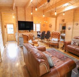 A living room with leather sofas and armchairs a rug a dining table with chairs and a wall-mounted TV at Bryn Derwen Lodge in Bethesda