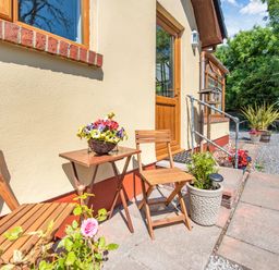 A small outdoor patio with wooden chairs and a table with flowers near a house entrance at Covert Farm Cwtch in Jeffreyston