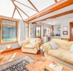 A living room with beige sofas and a wooden floor next to a kitchen and large windows at Covert Farm Cwtch in Jeffreyston