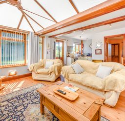 A living room with sofas a wooden coffee table a television and a kitchen in the background at Covert Farm Cwtch in Jeffreyston