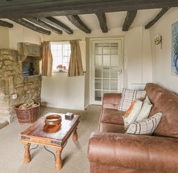 A living room with a brown leather sofa cushions a wooden coffee table a stone fireplace and wooden ceiling beams at Spring Cottage in Alkerton near Banbury