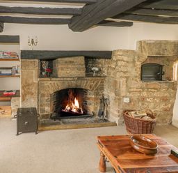 A living room with a stone fireplace a wooden coffee table and a television at Spring Cottage in Alkerton near Banbury