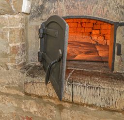 An open brick oven with a black metal door built into a stone wall at Spring Cottage in Alkerton near Banbury