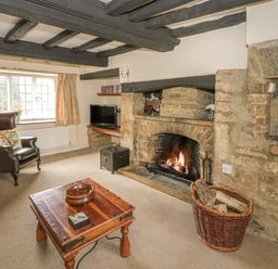 A living room with a stone fireplace burning fire a wooden table leather armchair and a television at Spring Cottage in Alkerton near Banbury