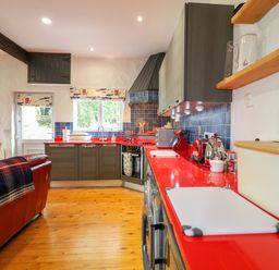 A kitchen with red countertops wooden floor grey cabinets and a red sofa at Quiet Waters Cottage in Loughan near Coleraine