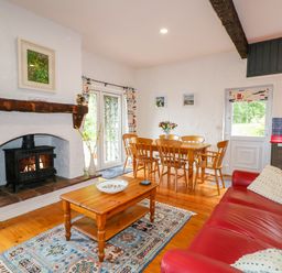 A living room with a red sofa wooden coffee table rug fireplace and dining table at Quiet Waters Cottage in Loughan near Coleraine