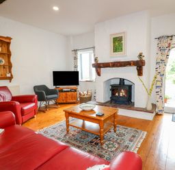 A living room with red leather sofas a wood burning stove a wooden coffee table and television at Quiet Waters Cottage in Loughan near Coleraine