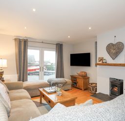A living room with a beige sofa a wooden coffee table a wall-mounted television and a fireplace at Laneton in Rhosneigr