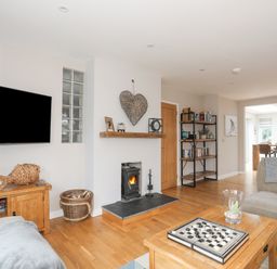 A living room with a wood burning stove a wooden coffee table and a sofa with a kitchen in the background at Laneton in Rhosneigr