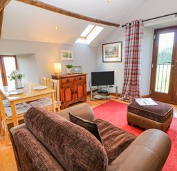 A living room with a brown sofa a wooden dining table with chairs a wooden cabinet a television and red rug at Field Barn in Alston