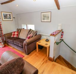 A living room with brown sofas plaid curtains a wooden side table and a staircase at Field Barn in Alston