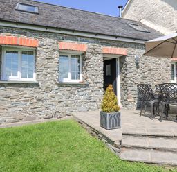 A stone house exterior with two windows a black door and outdoor seating with an umbrella at Yr Hen Beudy in Capel Bangor