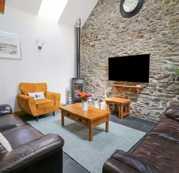 A living room with two leather sofas a yellow armchair wooden tables a wall clock and a stone wall at Yr Hen Beudy in Capel Bangor