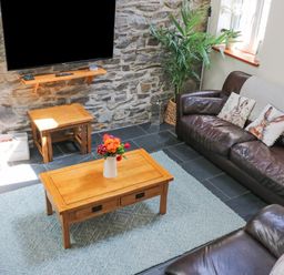 A living room with wooden tables leather sofas and a TV mounted on a stone wall at Yr Hen Beudy in Capel Bangor