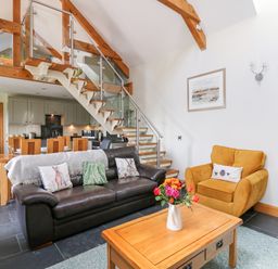 An open living room and kitchen area with a black leather sofa and a yellow armchair at Yr Hen Beudy in Capel Bangor