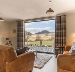 A living room with leather sofas a coffee table and a large window showing countryside at Cartref in Trawsfynydd