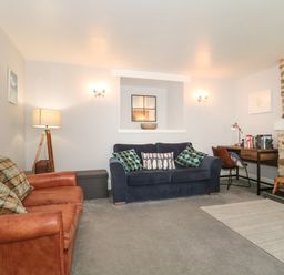 A living room with sofas a floor lamp a desk with a chair and a stone fireplace at The Linhay in Chardstock