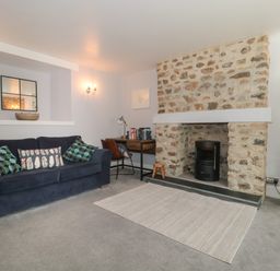 A living room with a blue sofa, stone fireplace, desk with chair, and a rug at The Linhay in Chardstock