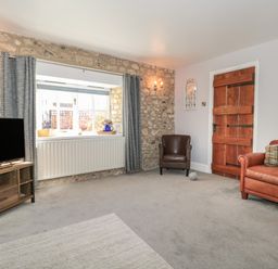 A living room with a stone wall window a brown leather armchair a wooden door a brown sofa and a television at The Linhay in Chardstock