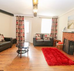 A living room with two black leather sofas a glass coffee table a red rug and a brick fireplace at Compass Cottage in Bodham near Sheringham