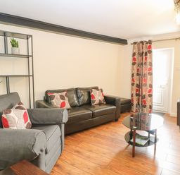 A living room with sofas coffee table shelves and patterned curtains at Compass Cottage in Bodham near Sheringham