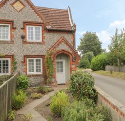 A brick and pebble stone cottage with white framed windows and a tiled roof beside a narrow road at Compass Cottage in Bodham near Sheringham
