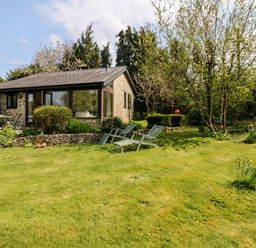 A garden with lawn chairs trees shrubs and a stone cottage at Puffin Cottage in Hawkchurch
