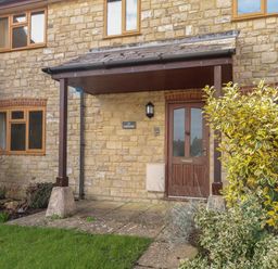 The front entrance of a stone house with a brown door and a small porch at Gabrianne in Burton Bradstock