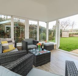 A sunroom with wicker furniture a glass coffee table and a view of a garden at Gabrianne Burton Bradstock