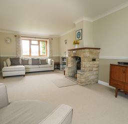 A living room with a stone fireplace a large sofa a wooden sideboard and a window with curtains at Gabrianne in Burton Bradstock