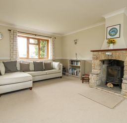 A living room with a beige sofa under a window a stone fireplace and a small bookshelf at Gabrianne in Burton Bradstock