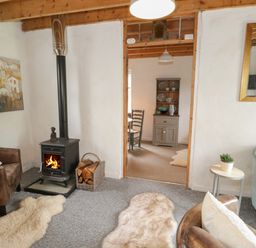 A living room with a wood burning stove chairs rugs and a view into a dining area at Little House in Red Wharf Bay