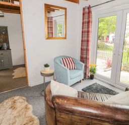 A living room with a leather sofa a blue armchair a small table with a plant a mirror on the wall and glass doors opening to a garden at Little House in Red Wharf Bay