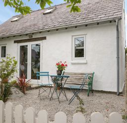 A small outdoor seating area with a table two chairs and a bench in front of a white house with a red door at Little House in Red Wharf Bay