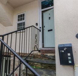 A staircase with black metal railing leading to a pale blue door with the number 1 the exterior wall has a mailbox and a plaque labeled Baileys 2 Cottages at 1 Bailey's Cottage in Stoke Fleming