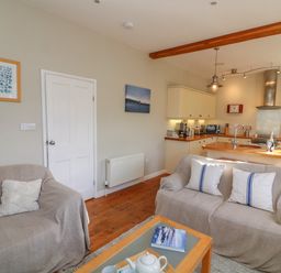 An open plan sitting area and kitchen with two sofas covered with throws and cushions at 1 Bailey's Cottage in Stoke Fleming
