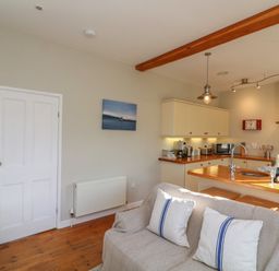 A kitchen and living area with wooden floors and a sofa with cushions at 1 Bailey's Cottage Stoke Fleming