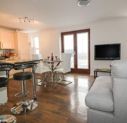 An open plan kitchen and living room with bar stools a dining table and a wall mounted television at Elin Howlyek in Newquay