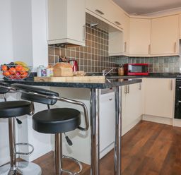 A kitchen with a breakfast bar and stools a fruit bowl bread toaster microwave and oven at Elin Howlyek in Newquay